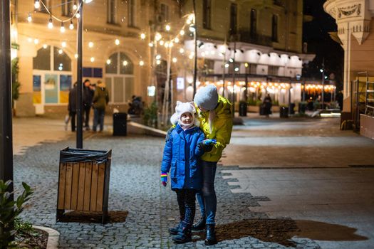 Mother with child girl at Christmas market celebrating New Year holiday. Family outdoor winter activity. Mom and daughter spend time together. Authentic lifestyle