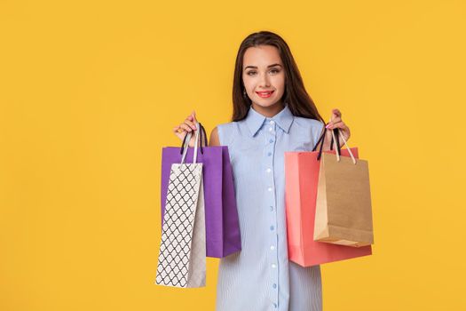 Young brunette lady in white and blue summer striped dress posing with shopping bags over yellow background.. Shopping. Sale