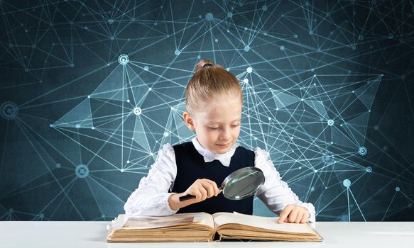 Little girl sitting at desk with magnifier and open book. Research and education in school. Happy schoolgirl in school wear carefully studying book. Clever girl reading book with magnifying glass.