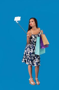 Young stylish woman posing and taking a selfie on the phone with shopping bags on a blue background. Emotions. Purchases. Sale. Shopping