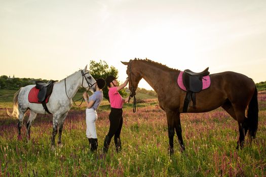 Two woman and two horses outdoor in summer happy sunset together nature. Taking care of animals, love and friendship concept.