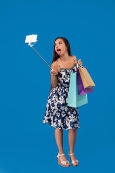 Young stylish woman posing and taking a selfie on the phone with shopping bags on a blue background. Emotions. Purchases. Sale. Shopping