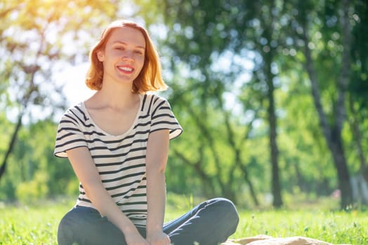 Portrait of a young attractive woman. Sitting cross-legged in the park