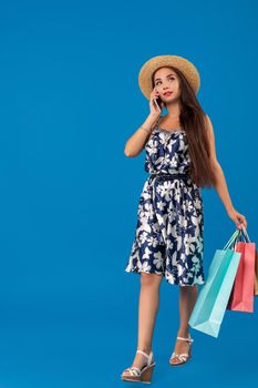 Shopping concept. Beautiful smiling brunette with shopping bags talking on the phone on blue studio background with copy space. Emotions. Emotional woman
