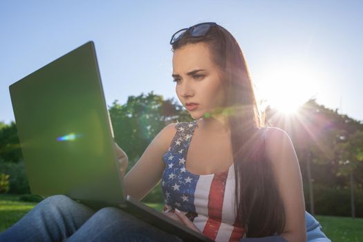 Pretty young woman sitting on bean bag use laptop while resting on grass in park on the sun. Success small business, modern lifestyle, information technology, or online shopping concept