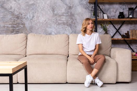 Young woman sitting on couch and relaxing at home, casual style indoor shoot. The blonde spends time at home