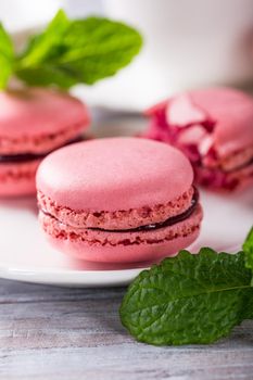 French raspberry macaroons with mint leaves on old white wooden background. Holidays food concept.