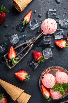 Flat lay with strawberry ice cream, berries and waffle cones on black background. Top view.