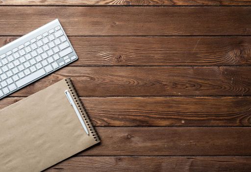 Still life of office workspace with supplies. Flat lay old wooden desk with white computer keyboard, pen and notebook. Top view business concept. Vintage brown wooden surface with copy space.