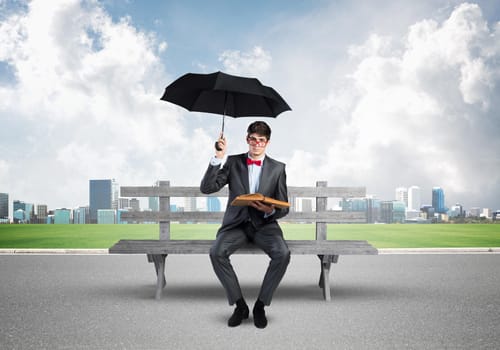 young student with umbrella and book sits on a bench