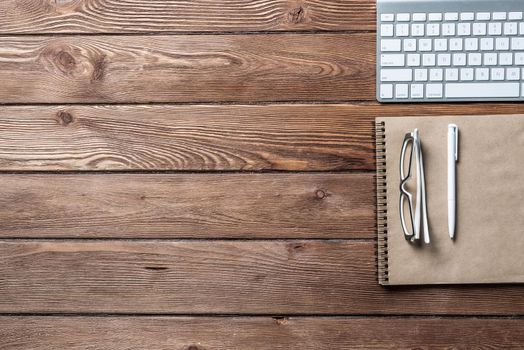 Top view of modern businessman workplace. Spiral notepad and computer keyboard on brown wooden surface. Education, creativity and innovation concept with copy space. Flat lay vintage office workspace