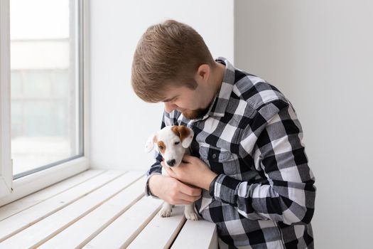 people, pets and animals concept - young man hugging puppy near window on white background.