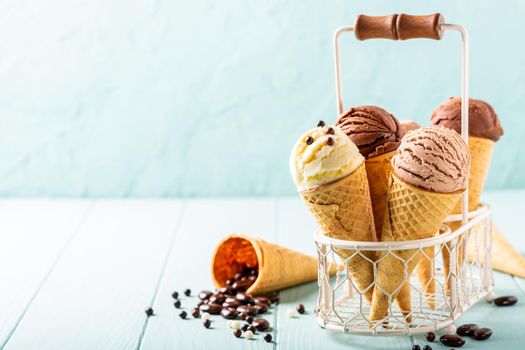 Waffle cones with homemade coffee, vanilla and chocolate ice cream on turquoise background. Healthy summer food concept with copy space.