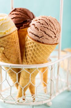 Homemade coffee, vanilla and chocolate ice cream in waffle cones on turquoise background. Healthy summer food concept.