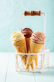 Waffle cones with homemade coffee, vanilla and chocolate ice cream on turquoise background. Healthy summer food concept with copy space.