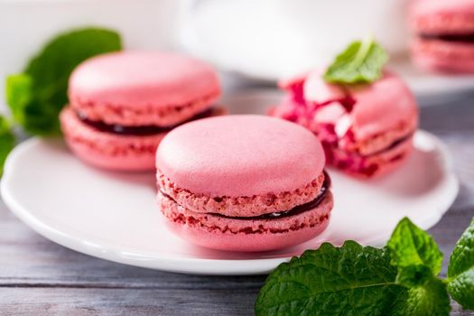 French raspberry macaroons with mint leaves on old white wooden background. Holidays food concept.