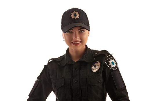 Close-up shot of a cute redheaded policewoman in a black uniform and a cap looking at the camera and smiling, isolated on white background. Defender of citizens is ready to enforce a law and stop a crime.