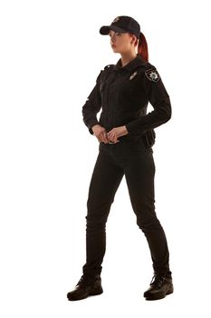 Full length shot of a beautiful ginger lady police officer in a uniform and a cap posing sideways for the camera, isolated on white background. Defender of citizens is ready to enforce a law and stop a crime.