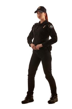 Full length shot of a beautiful redhead maiden police officer in a uniform and a cap posing sideways and looking at the camera, isolated on white background. Defender of citizens is ready to enforce a law and stop a crime.