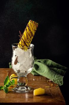 Delicious homemade pineapple in chocolate popsicle in glass on wooden table. Summer food concept with copy space. Dark photo