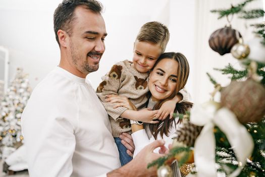 Family of 3 decorating a Christmas tree at home, close up