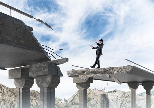 Businessman walking blindfolded on concrete bridge with huge gap as symbol of hidden threats and risks. Skyscape and nature view on background. 3D rendering.