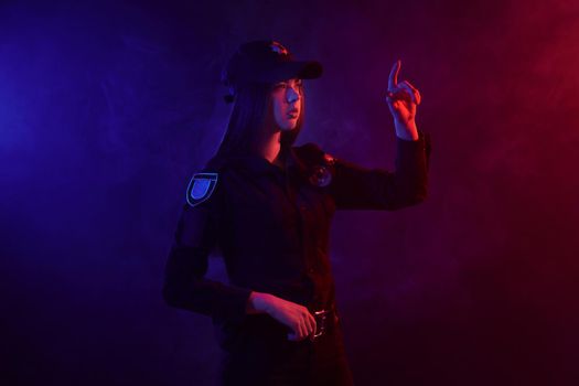 Charming redheaded woman traffic controller in a uniform and a cap is regulating traffic with signals standing sideways against a black background with red and blue backlighting. Defender of citizens is ready to enforce a law and stop a crime.