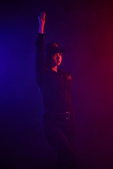Charming redheaded lady traffic controller in a uniform and a cap is regulating traffic with signals against a black background with red and blue backlighting. Defender of citizens is ready to enforce a law and stop a crime.