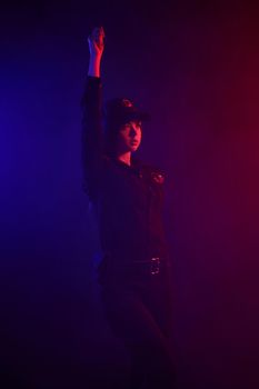 Charming redheaded lady traffic controller in a uniform and a cap is regulating traffic with signals against a black background with red and blue backlighting. Defender of citizens is ready to enforce a law and stop a crime.