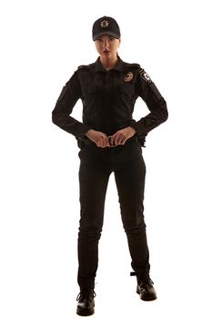 Full length shot of a beautiful redheaded girl police officer in a uniform and a cap holding her belt and looking seriosly at the camera, isolated on white background. Defender of citizens is ready to enforce a law and stop a crime.