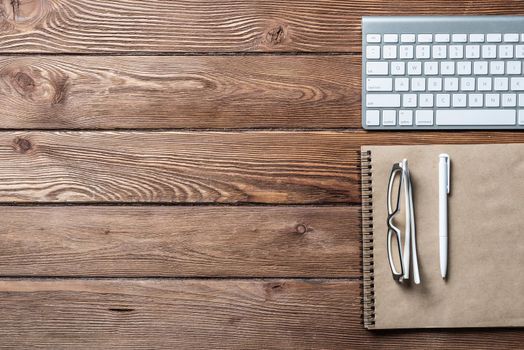 Top view of modern businessman workplace. Spiral notepad and computer keyboard on brown wooden surface. Education, creativity and innovation concept with copy space. Flat lay vintage office workspace