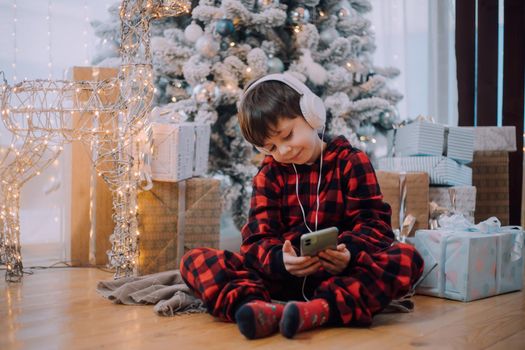 The boy with the phone under the Christmas tree lifestyle. New Year and Christmas. Festive decoration.