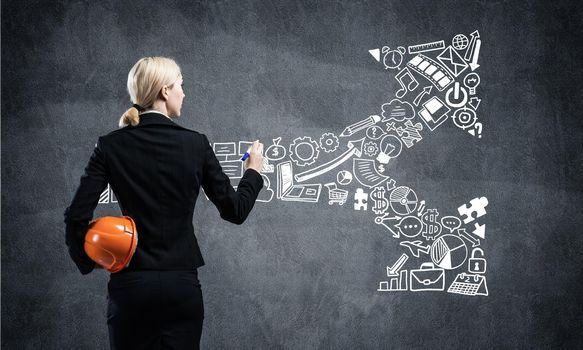 Businesswoman draws arrows consists of business doodles on blackboard. Personal success and career ambition. Back view woman with safety helmet. Strategy planning and project management concept.