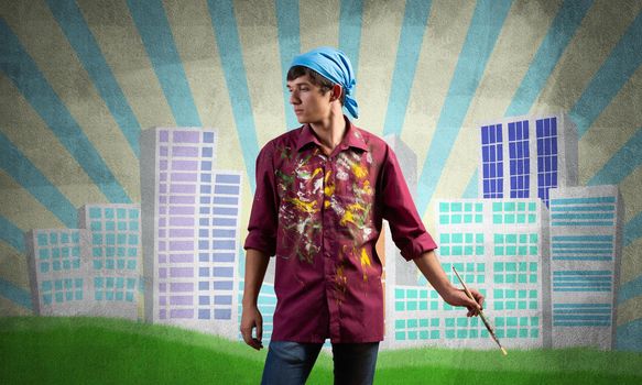 Young male artist holding paintbrush. Painter in shirt and bandana standing on background colorful picture on wall. Modern cityscape with high skyscrapers artwork. Creative hobby and profession