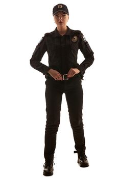 Full length shot of a beautiful redheaded female police officer in a uniform and a cap holding her belt and looking at the camera, isolated on white background. Defender of citizens is ready to enforce a law and stop a crime.
