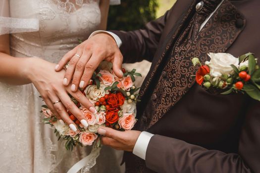 The bride and groom put their hands on the wedding decorative bouquet of flowers of roses close-up.
