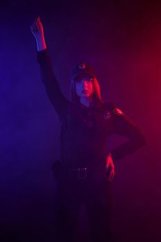 Charming redheaded girl traffic controller in a uniform and a cap is looking at the camera and regulating traffic with signals against a black background with red and blue backlighting. Defender of citizens is ready to enforce a law and stop a crime.