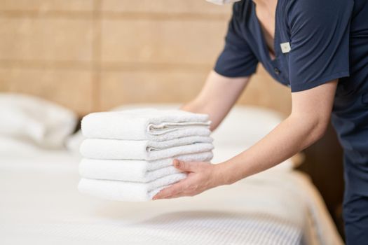 Cropped photo of maid in uniform holding stack of clean towels in room in hotel. Hotel service concept