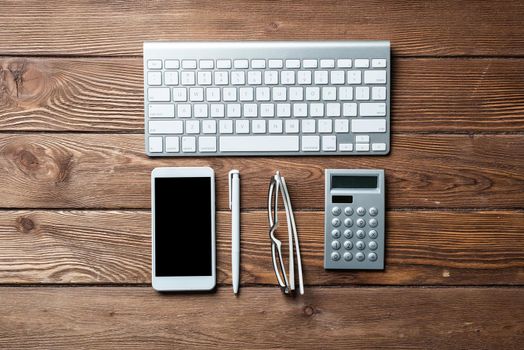 Top view of accountant workspace with office accessories. Flat lay wooden desk with computer keyboard, calculator and smartphone. Accounting and banking services. Finance and investment concept.