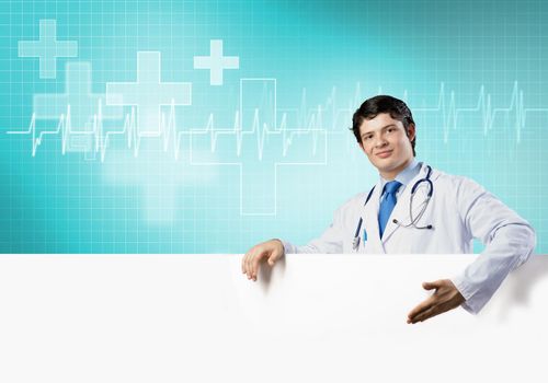 Young handsome doctor holding white blank banner. Place your text