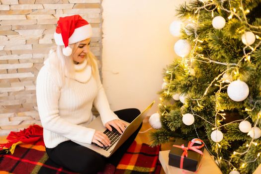 Photo of a beautiful blond female sitting on a couch using a laptop to shop for Christmas gifts.