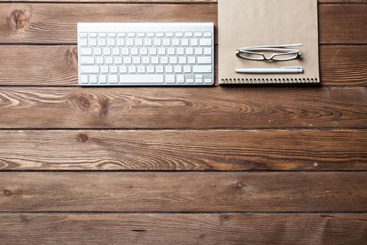 Top view of modern businessman workplace. Spiral notepad and computer keyboard on brown wooden surface. Education, creativity and innovation concept with copy space. Flat lay vintage office workspace