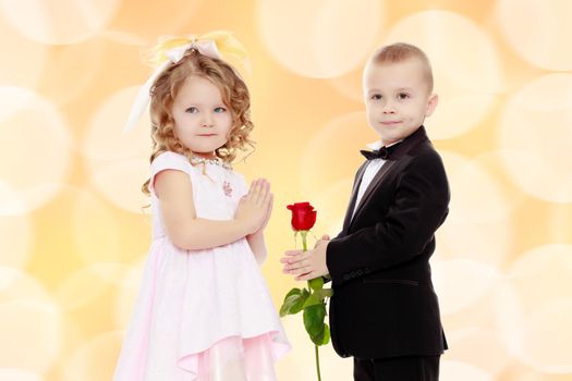 Little boy in black suit with bow tie gives a big red rose charming little girl.Brown festive, Christmas background with white snowflakes, circles.