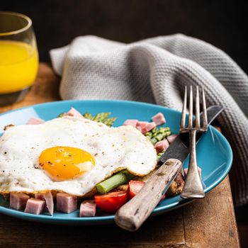 Healthy breakfast or lunch with fried egg, bread toast, green asparagus and tomatoes on blue plate on old wooden table