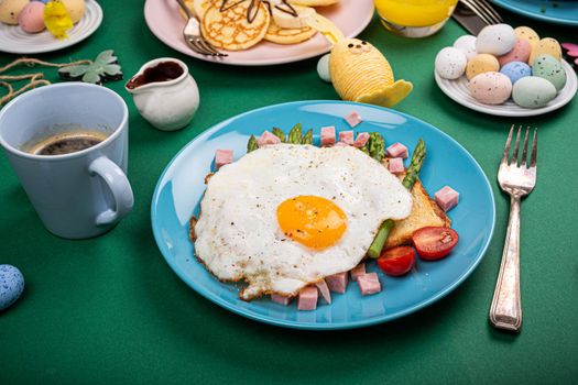 Breakfast or lunch with fried egg, bread toast, green asparagus, tomatoes and bacon on blue plate.