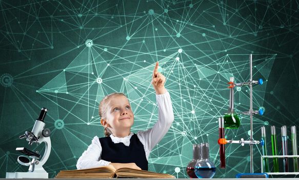 Little girl scientist sitting at desk in elementary science class. Research and education in school. Chemical laboratory with microscope, flasks and test tubes. Happy schoolgirl finger pointing up