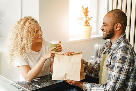 Smiling blonde woman talking to a waiter of a coffee shop at the counter table