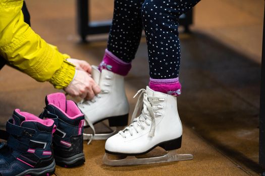 Woman is helping her daughter put her figure skates on before she takes her to a skating lesson