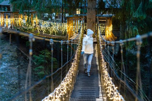 woman on suspension bridge in the evening among Christmas lights.