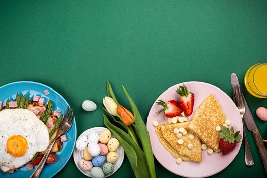 Easter composition with breakfast flat lay with scrambled eggs bagels, tulips, pancakes, bread toast with fried egg and green asparagus, colored quail eggs. Top view. Copy space.